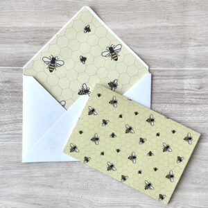 An envelope and matching card with a a bee pattern and yellow background background on a table