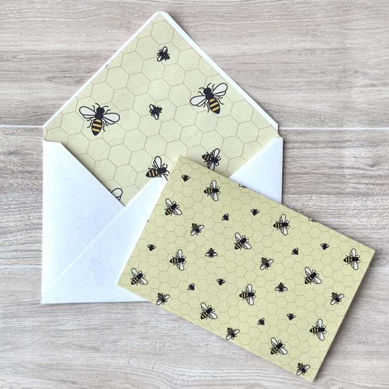 An envelope and matching card with a a bee pattern and yellow background background on a table