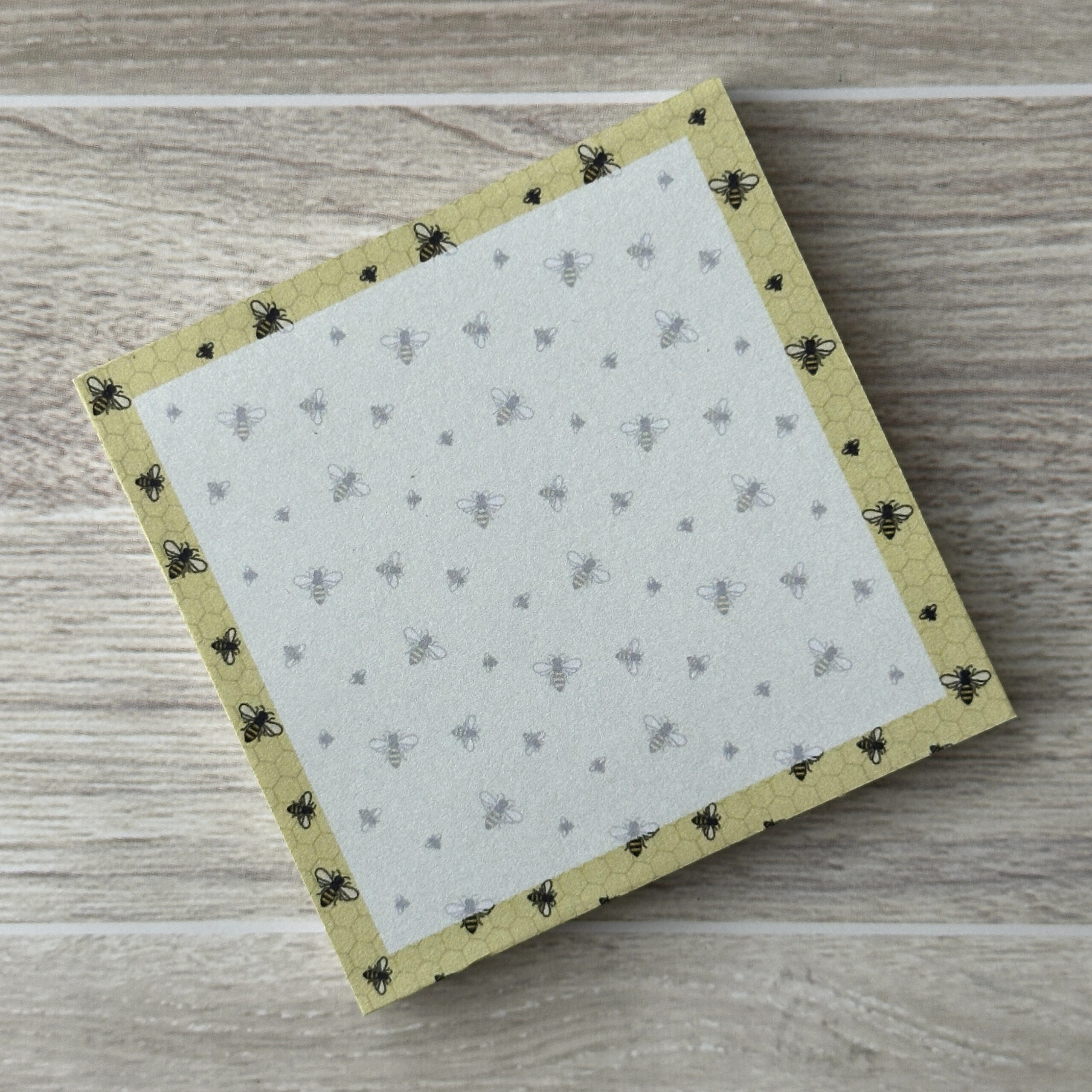 A square sticky notepad with a pattern of bees and a yellow border