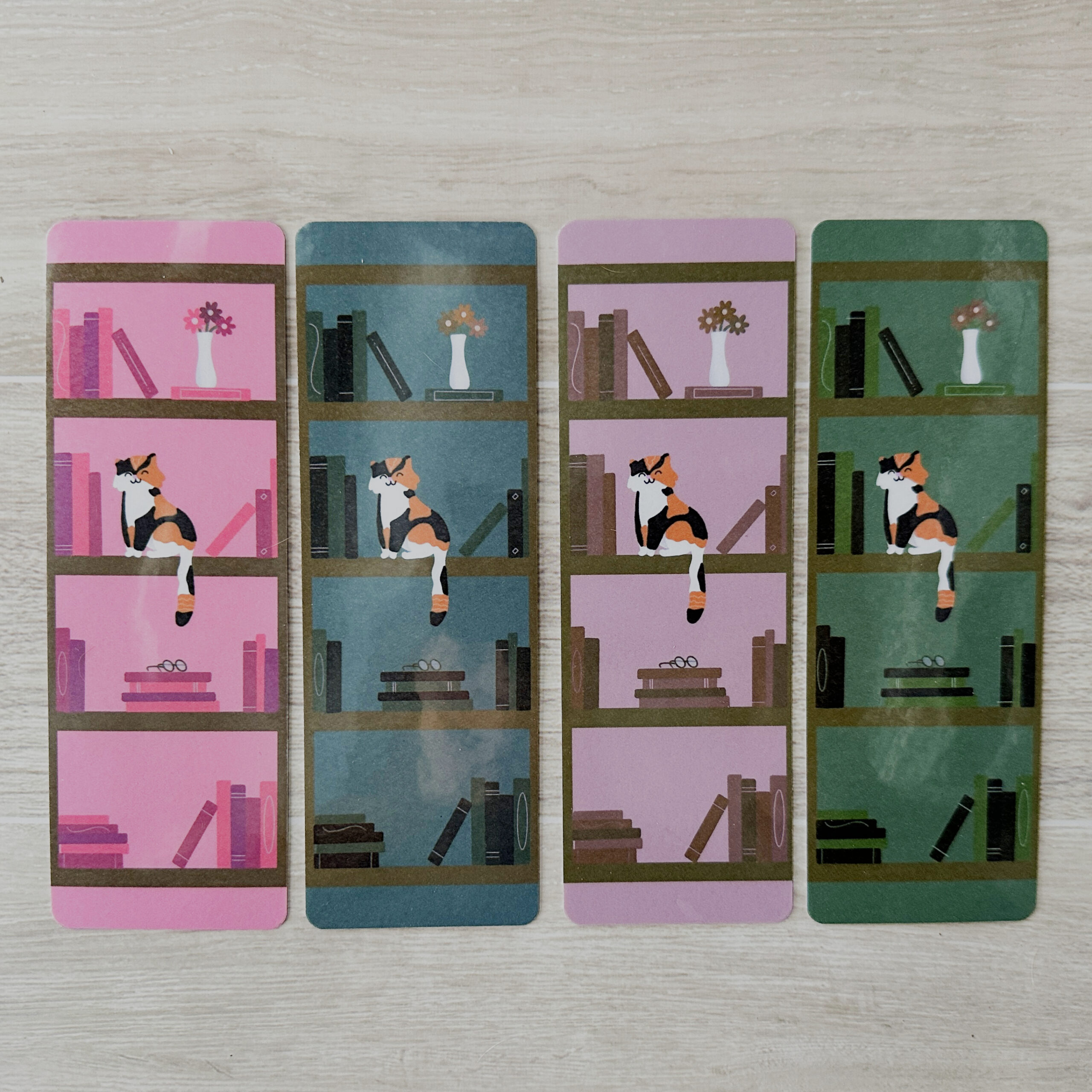 4 bookmarks sporting a bookshelf and a cat each with a different colored background - pink, blue, purple, green from left to right.