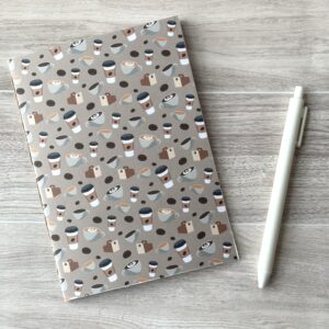 A notebooklet with an assorted coffee items pattern sits on a table with a white pen