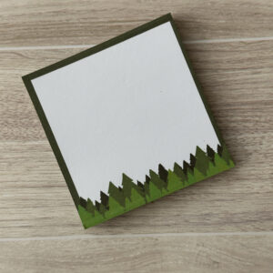 A square sticky notepad with assorted green pine trees along the bottom and a dark green border