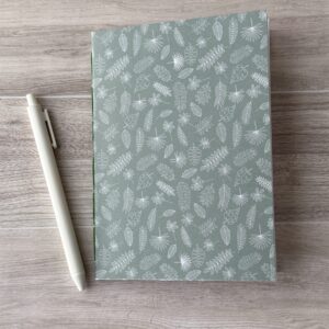 A notebooklet with an assorted leaves pattern sit on a table with a white pen