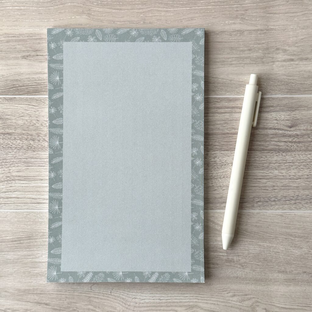 A paper pad with an assorted leaves pattern sit on a table with a white pen
