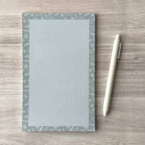 A paper pad with an assorted leaves pattern sit on a table with a white pen