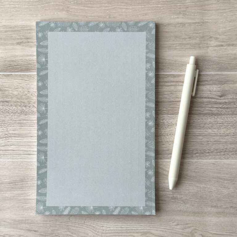 A paper pad with an assorted leaves pattern sit on a table with a white pen