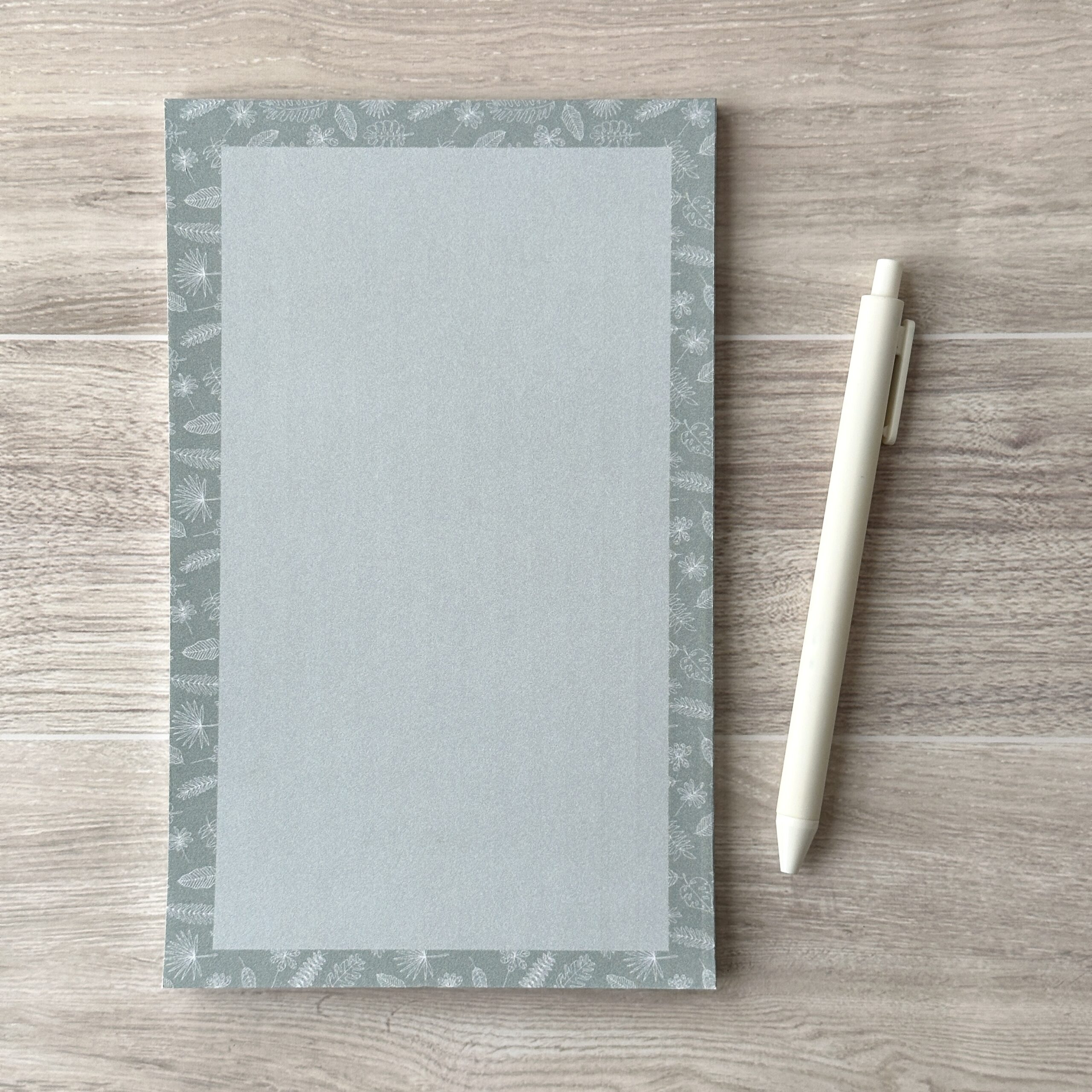 A paper pad with an assorted leaves pattern sit on a table with a white pen