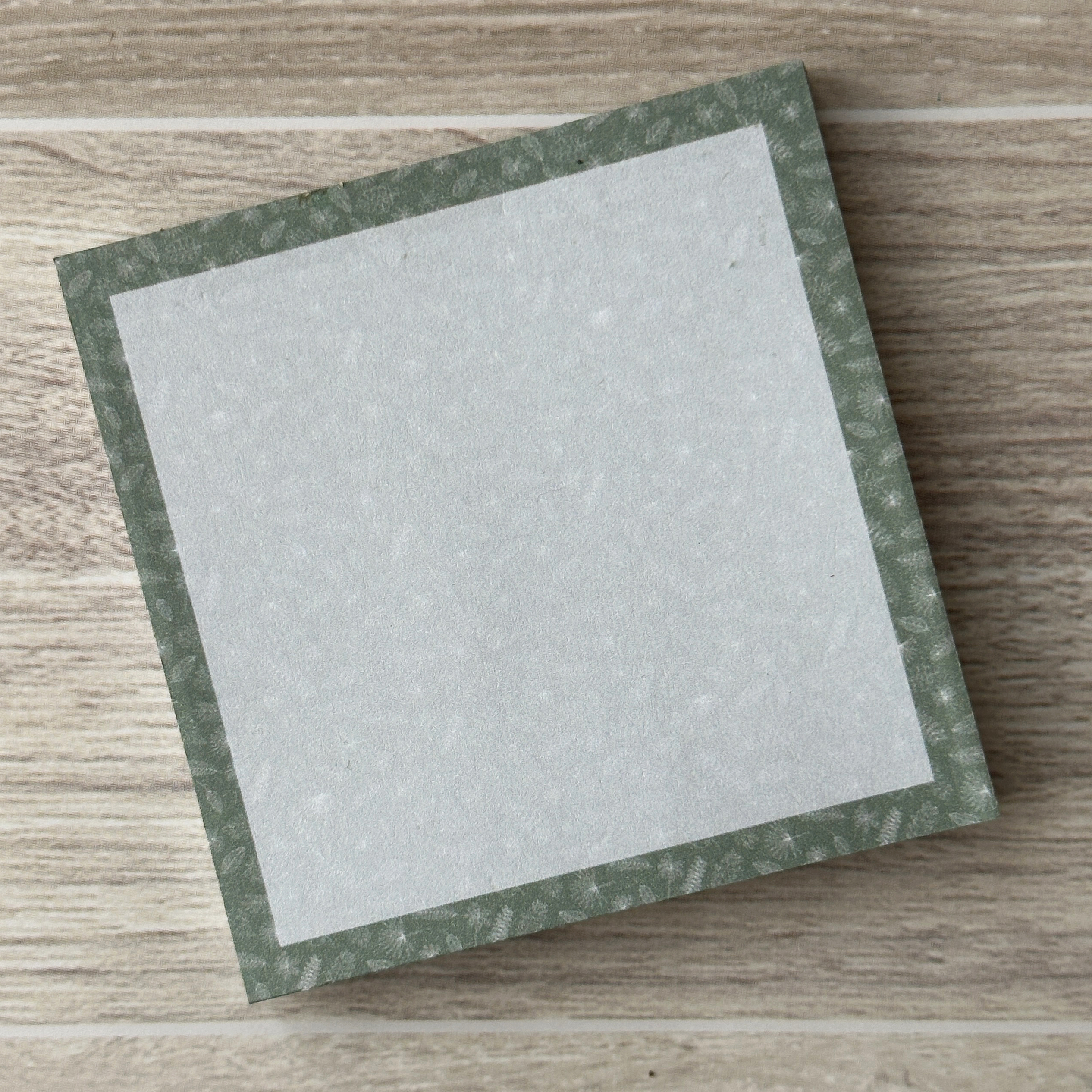a square sticky notepad with an assortment of white leaves along the border with a soft green background