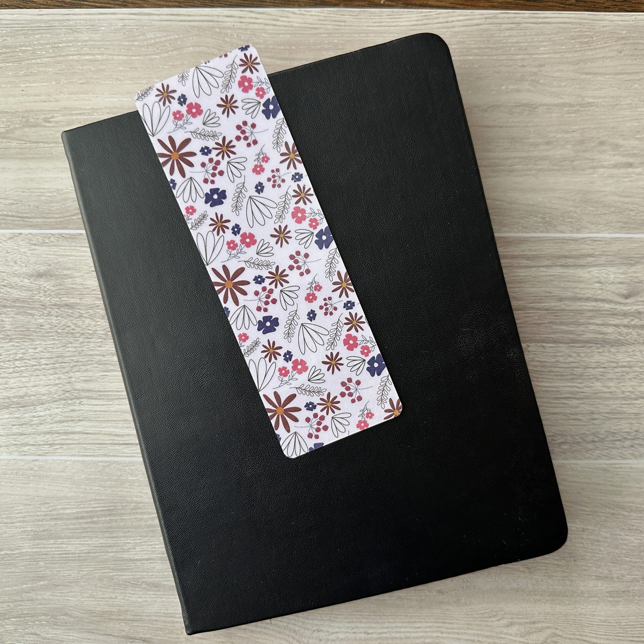 A bookmark with a pink floral pattern rests atop a black notebook