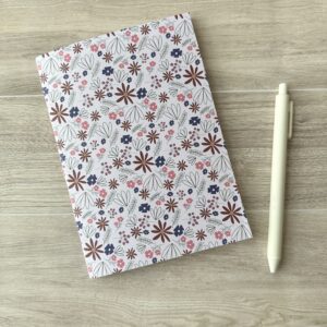 A notebooklet with a pink floral pattern sits on a table with a white pen