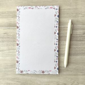 A paper pad with a pink floral pattern sits on a table with a white pen