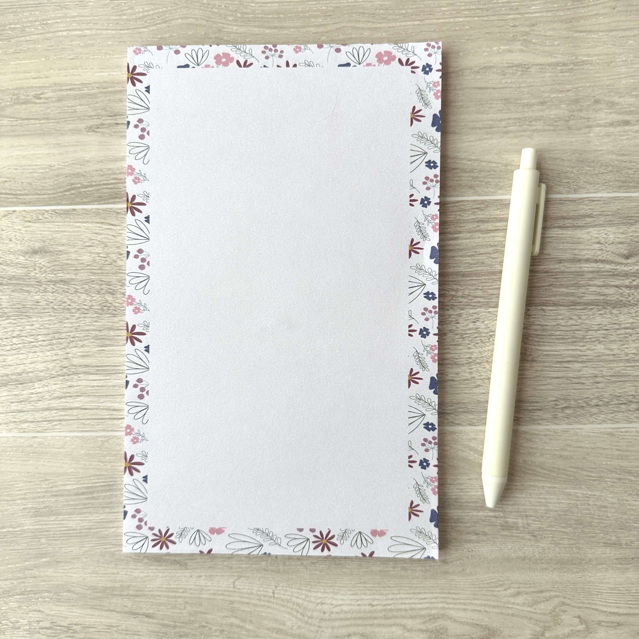 A paper pad with a pink floral pattern sits on a table with a white pen