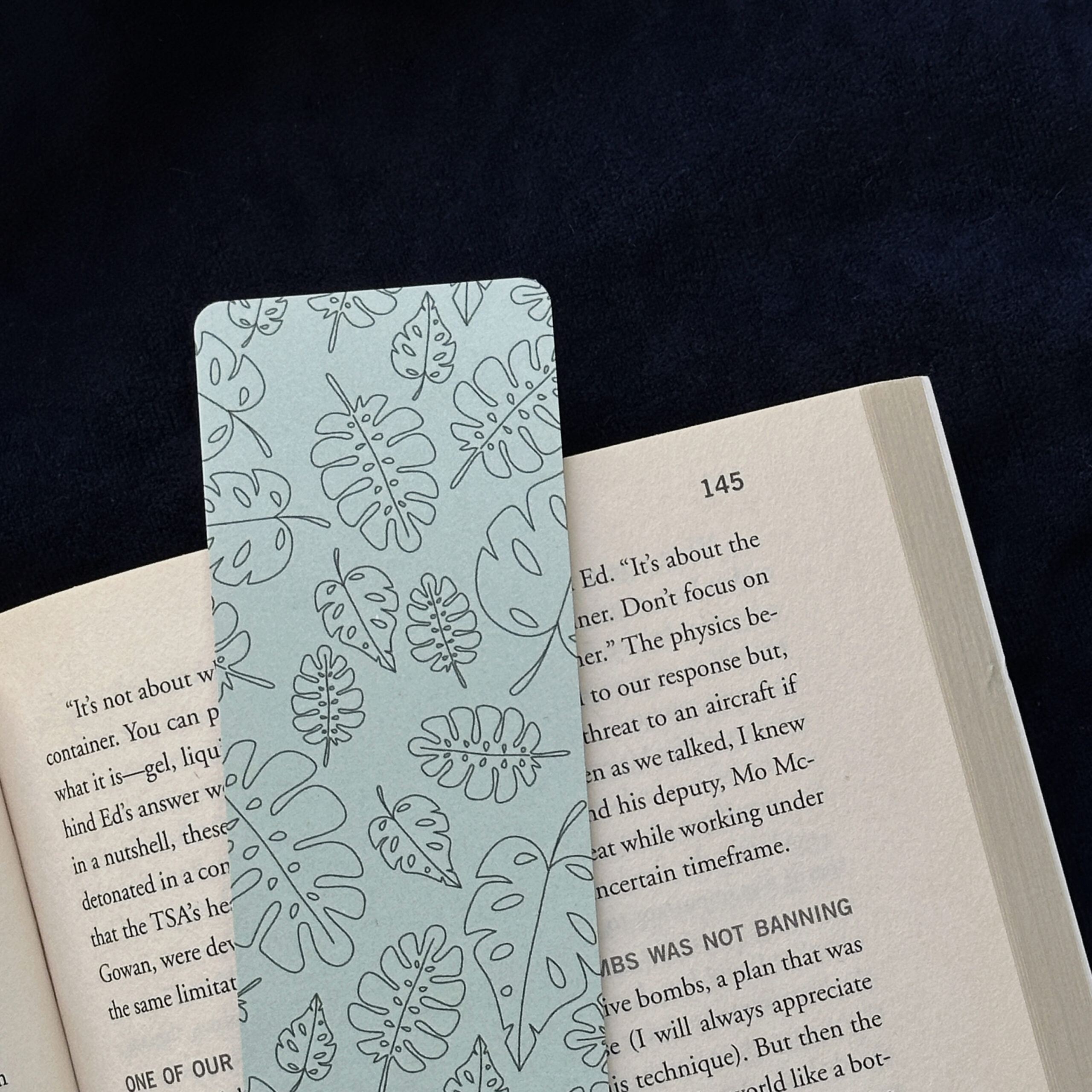 A bookmark with assorted tropical leaves and a green background rests upon the pages of an open book.