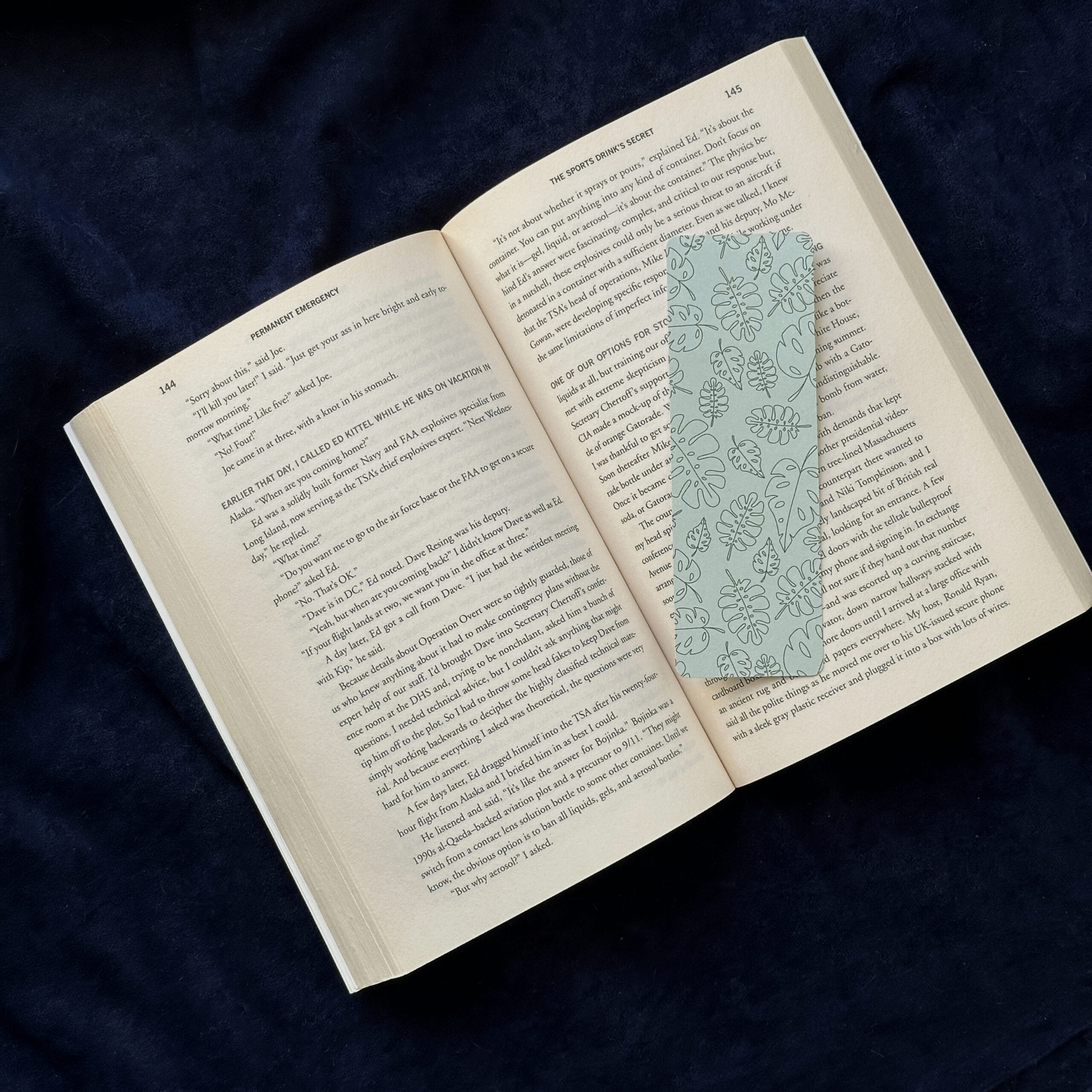 A bookmark with assorted tropical leaves and a green background rests upon the pages of an open book.